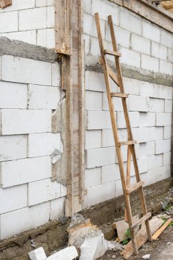 Duvara dayanmış tahta merdiven. Merdiven tuğladan yapılmış bir duvara dayanıyor. Tuğlalar beyaz ve merdiven kahverengi.