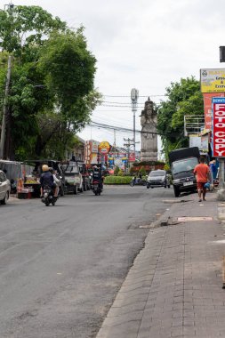 Bali, Endonezya - 29 Aralık 2024: Turuncu gömlekli bir adamla dolu bir cadde. Sokakta birkaç motosiklet ve araba var.