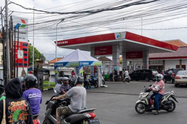 Bali, Endonezya - 29 Aralık 2024: Pertamina benzin istasyonu. Erkek ve kadın bir benzin istasyonunun önünde motosiklet sürüyor. Adam kask takıyor.