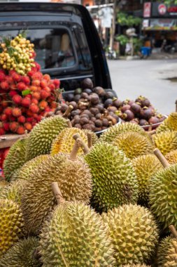 Durian yığını bir pazarda sergileniyor. Durianlar çok yüksektir ve etrafları başka meyvelerle çevrilidir.