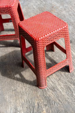 İki kırmızı plastik tabure ahşap bir zeminde oturuyor. Tabureler şekil ve boyut olarak aynı.