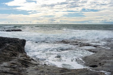 Büyük bir dalganın kayalara çarptığı kıyı şeridi. Su dalgalı ve kayalar yosunla kaplı. Sahne güç ve güçten oluşur.
