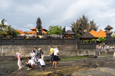Bali, Endonezya - 29 Aralık 2024: Birçok turist Tanah Lot turistik beldesini ziyaret ediyor. Sahilde, bir kaya oluşumunun yakınında toplandılar..