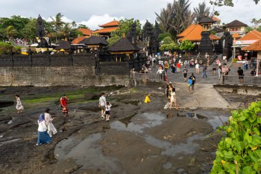 Bali, Endonezya - 29 Aralık 2024: Birçok turist Tanah Lot turistik beldesini ziyaret ediyor. Sahilde, bir kaya oluşumunun yakınında toplandılar..