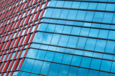 Arka planda mavi gökyüzü ve kırmızı pencereli bina. Mavi gökyüzü açık ve bina yüksek.