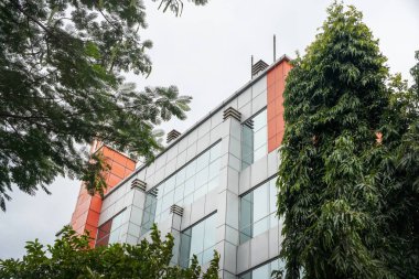 Önünde yeşil bir ağaç olan yüksek bir bina. Bina camdan yapılmıştır ve kırmızı bir çatısı vardır.