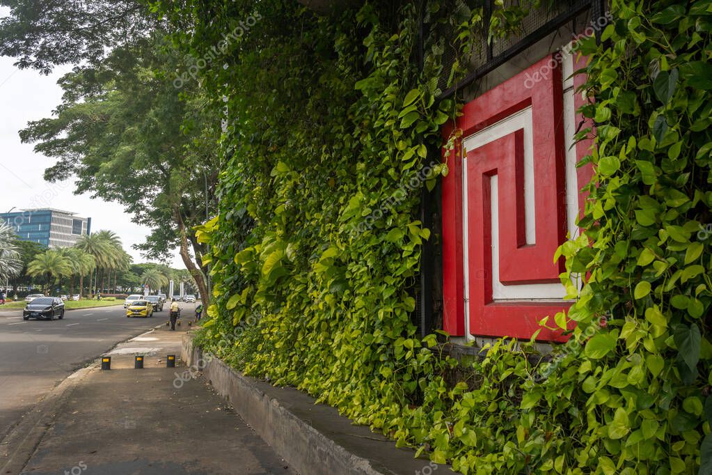 Wall covered in ivy and plants with a Bintaro Jaya logo. The wall is green and red with a white trim