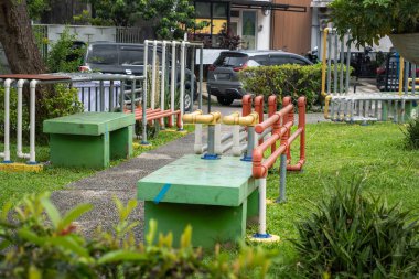 Yeşil banklı ve kırmızı banklı bir park. Bankın etrafı borularla çevrili.