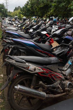 Birçok motosiklet sürüsü park halindedir. Motosikletler çeşitli boyut ve renklerde ve hepsi sıra sıra dizilmiş. Sahne bir düzen hissi veriyor.