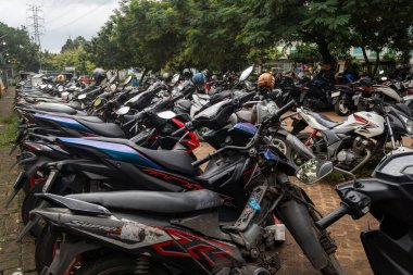 Birçok motosiklet sürüsü park halindedir. Motosikletler çeşitli boyut ve renklerde ve hepsi sıra sıra dizilmiş. Sahne bir düzen hissi veriyor.
