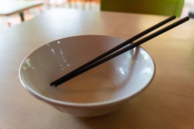 Üstünde çubuklar olan bir kase yemek. Kase boş ve yemek çubukları siyah.