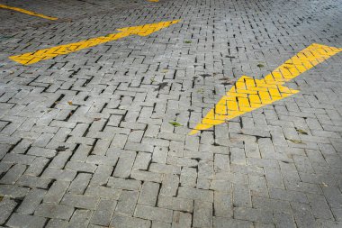 Sağda sarı oklar olan tuğla yol. Yol boş ve üzerinde ne araba ne de insan var. Oklar doğru yöne doğru yerleştirilmiştir.