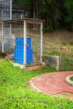 Mavi fıçı bir çitin önünde oturuyor. Çit metalden yapılmıştır ve bir tepededir.