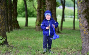 Mutlu çocuk bir kar oyuncağı taşıyor ve soğuk bir bahar gününde parkta yürüyor. Küçük çocuk dişleriyle gülümsüyor ve dışarıda oynuyor..