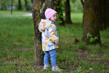 Soğuk baharda parkta yürüyen kot pantolonlu küçük bir kız. Küçük kız parkta doğayı keşfediyor..