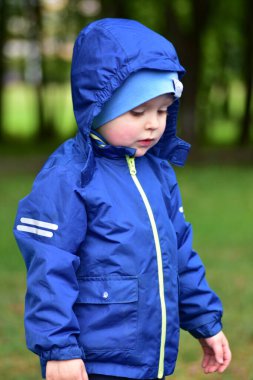 İlkbaharda parkta küçük çocukların portresi. Kapüşonlu küçük çocuk dışarıdaki tablonun içine bakıyor..