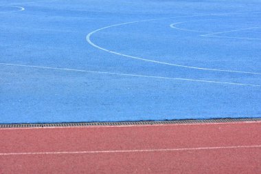 Kırmızı koşu pisti ve mavi spor sahası. Altta kırmızı stadyum koşu pisti olan boş bir basketbol sahası.
