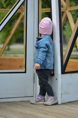 Baharda terasta dikilen gri kotlu yüzsüz küçük kız. Küçük kız boş bina duvarının yanında isimsiz poz veriyor..