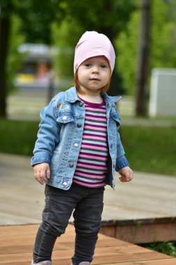 Baharda terasta dikilen gri kotlu küçük kız. Küçük kız parkta poz veriyor..