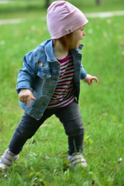 Gri kotlu küçük kız baharda parkta çimenlerde mutlu bir şekilde koşuyor. Küçük kız parkta eğleniyor..