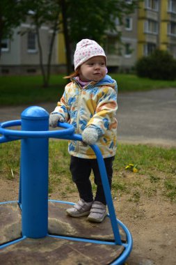 Soğuk havalarda eski Sovyet apartmanlarının yanında dönen ekipmanların üzerinde duran komik taklitçi küçük bir kız. Küçük kız sosyalist dönemin ortak alanlarında dönerek eğleniyor..