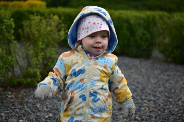 Dili açık, ağzı açık, küçük kayalarla dolu bir parkta yürüyen küçük bir kız. Komik taklitleri olan küçük bir kız halka açık oyun parkında portreye çıkıyor..