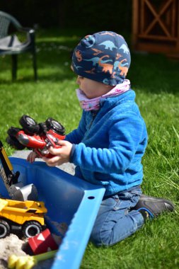 Küçük çocuk arka bahçedeki küçük bir kum havuzunda oyuncaklarla oynuyor. Çocuk bahar vakti dışarıda eğleniyor..