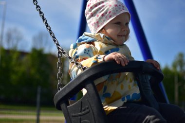Yavru kız, baharda şehir parkındaki çocuk parkında sallanmaktan mutlu. Küçük kız güneşli baharda halk parkında eğleniyor..