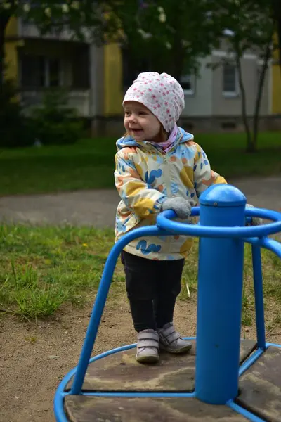 Soğuk havalarda eski Sovyet apartmanlarının yanında dönen ekipmanların üzerinde duran komik taklitçi küçük bir kız. Küçük kız sosyalist dönemin ortak alanlarında dönerek eğleniyor..