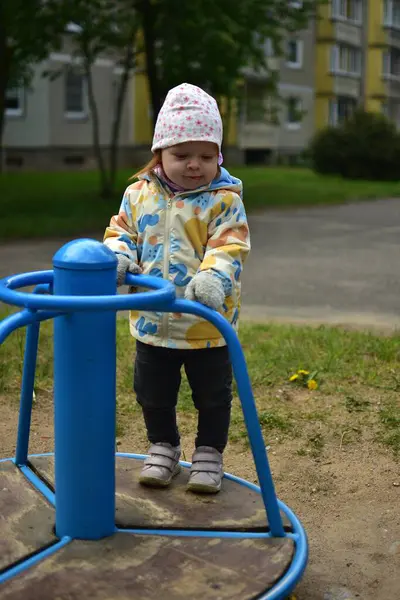 Soğuk havalarda eski Sovyet apartmanlarının yanında dönen ekipmanların üzerinde duran komik taklitçi küçük bir kız. Küçük kız sosyalist dönemin ortak alanlarında dönerek eğleniyor..