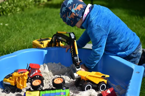 Küçük çocuk arka bahçedeki küçük bir kum havuzunda oyuncak kazıcısıyla oynuyor. Çocuk bahar vakti dışarıda eğleniyor..