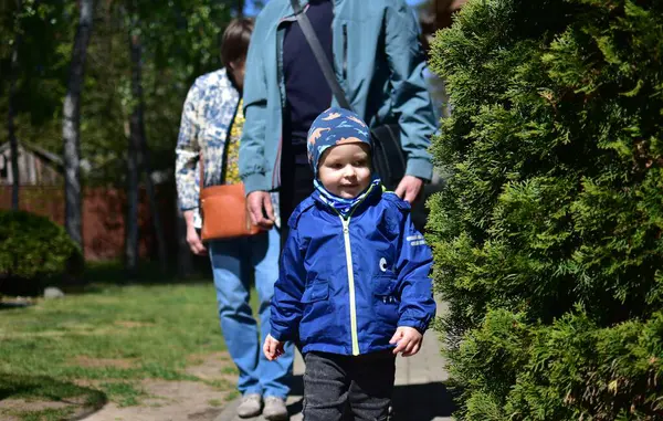 Küçük çocuk güneşli bahar gününde büyükannesi ve büyükbabasıyla birlikte dışarıda yürüyor. Küçük çocuk parkta yürüyüşe çıkıyor..