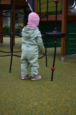 Yavru kız, baharda şehir parkındaki çocuk parkında tırmanma ağıyla oynuyor. Çocuk halk parkında ip ekipmanına tırmanmaya çalışıyor..