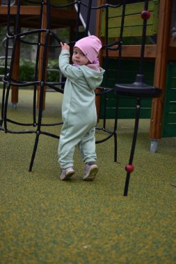 Yavru kız, baharda şehir parkındaki çocuk parkında tırmanma ağıyla oynuyor. Çocuk halk parkında ip ekipmanına tırmanmaya çalışıyor..