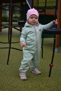 Yavru kız, soğuk baharda şehir parkındaki çocuk parkında ip tırmanışı yapıyor. Çocuk halk parkında ip ekipmanına tırmanmaya çalışıyor..