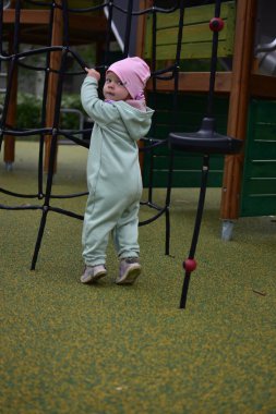 Yavru kız, baharda şehir parkındaki çocuk parkında tırmanma ağıyla oynuyor. Çocuk halk parkında ip ekipmanına tırmanmaya çalışıyor..