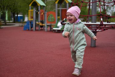 Yavru kız, baharda şehir parkındaki çocuk parkında oynarken çok mutlu. Küçük kız bulutlu bir baharda halk parkında anlamlı bir şekilde yürüyor..