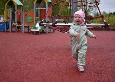 Yavru kız, baharda şehir parkındaki çocuk parkında oynarken çok mutlu. Küçük kız bulutlu bir baharda halk parkında anlamlı bir şekilde yürüyor..