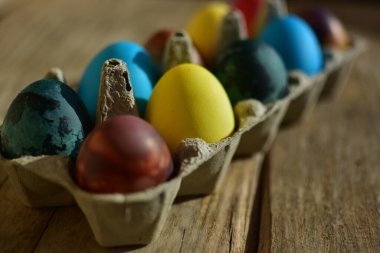 Kırık ahşap arka planda kağıt bir kutunun içindeki renkli paskalya yumurtaları. Geleneksel Avrupa paskalya yumurtaları güneşli bir günde manzarayı kapatır.