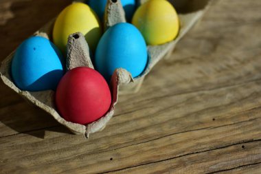 Kırık ahşap arka planda kağıt bir kutunun içindeki renkli paskalya yumurtaları. Geleneksel Avrupa paskalya yumurtaları güneşli bir günde manzarayı kapatır.