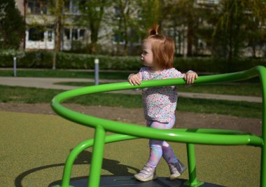 Şehir parkındaki çocuk parkında bahar havasında dönen ekipmanların üzerinde duran küçük kız. Küçük kız güneşli bir baharda halk parkında dönerek eğleniyor..