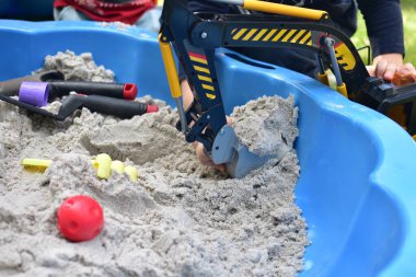 Küçük çocuk arka bahçedeki küçük bir kum havuzunda oyuncak kazıcısıyla oynuyor. Yazın dışarıda eğlenen bir çocuk. Yüzü yok