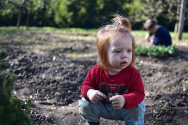 Yavru kız baharda arka bahçede toprakla oynuyor. Güneşli bir günde toprağın altında oynayan edepsiz görünümlü bir kız. Arka plandaki kardeş..