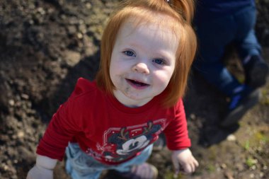 Sümüklü burunlu ve kirli yüzlü küçük kız baharda bir bahçede gülümsüyor..