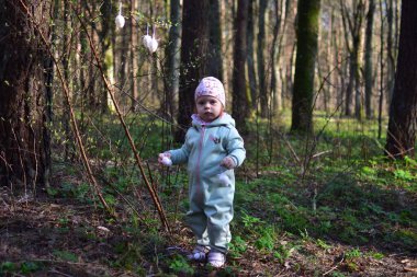 Küçük kız ormandaki çalılara paskalya yumurtası süslemesi asıyor. Küçük kız parkta paskalya yumurtası süslemeleriyle oynuyor. Çocukların Paskalya tatiline hazırlanması kavramı.