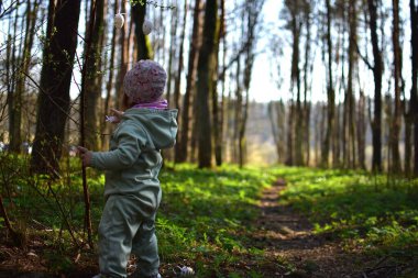Küçük kız ormandaki çalılara paskalya yumurtası süslemesi asıyor. Küçük kız parkta paskalya yumurtası süslemeleriyle oynuyor. Çocukların Paskalya tatiline hazırlanması kavramı.
