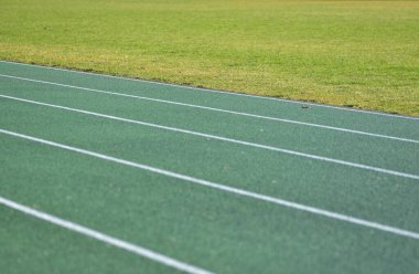 Beyaz çizgileri ve sağ tarafında yeşil çimenler olan yeşil koşu pisti. Okul stadyumu spor pisti.