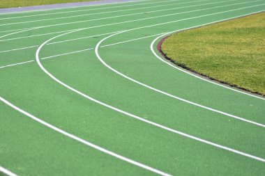 Beyaz çizgileri olan yeşil koşu yolu eğrisi. Sol tarafta patika, sağ tarafta yeşil çim. Okul stadyumu spor pisti.