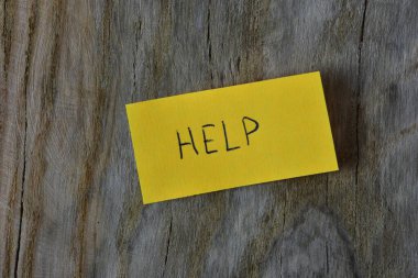 Tahta döşemeli arka plandaki sarı yapışkan nota mesaj yardımı. Mavi kalem kağıt üzerine kelime yardımı yazdı.