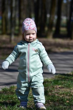 Baharda bir parkta naneli, yumuşak kabuklu bir elbise giyen bebek oynuyor. Gülümseyen küçük kız çimlerin üzerinde yürüyor.